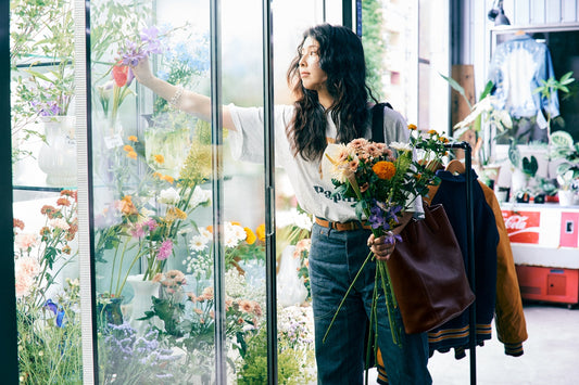A woman holding flowers and a Tsuchiya Kaban leather tote bag while choosing flowers.