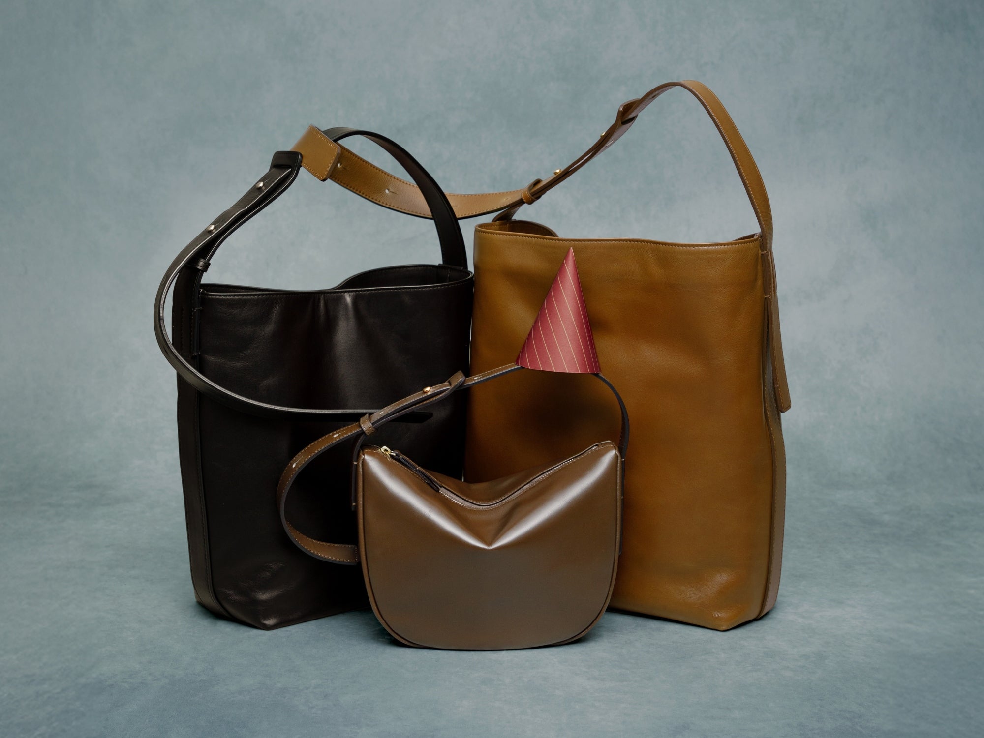 Three leather handbags in brown and black on a gray background