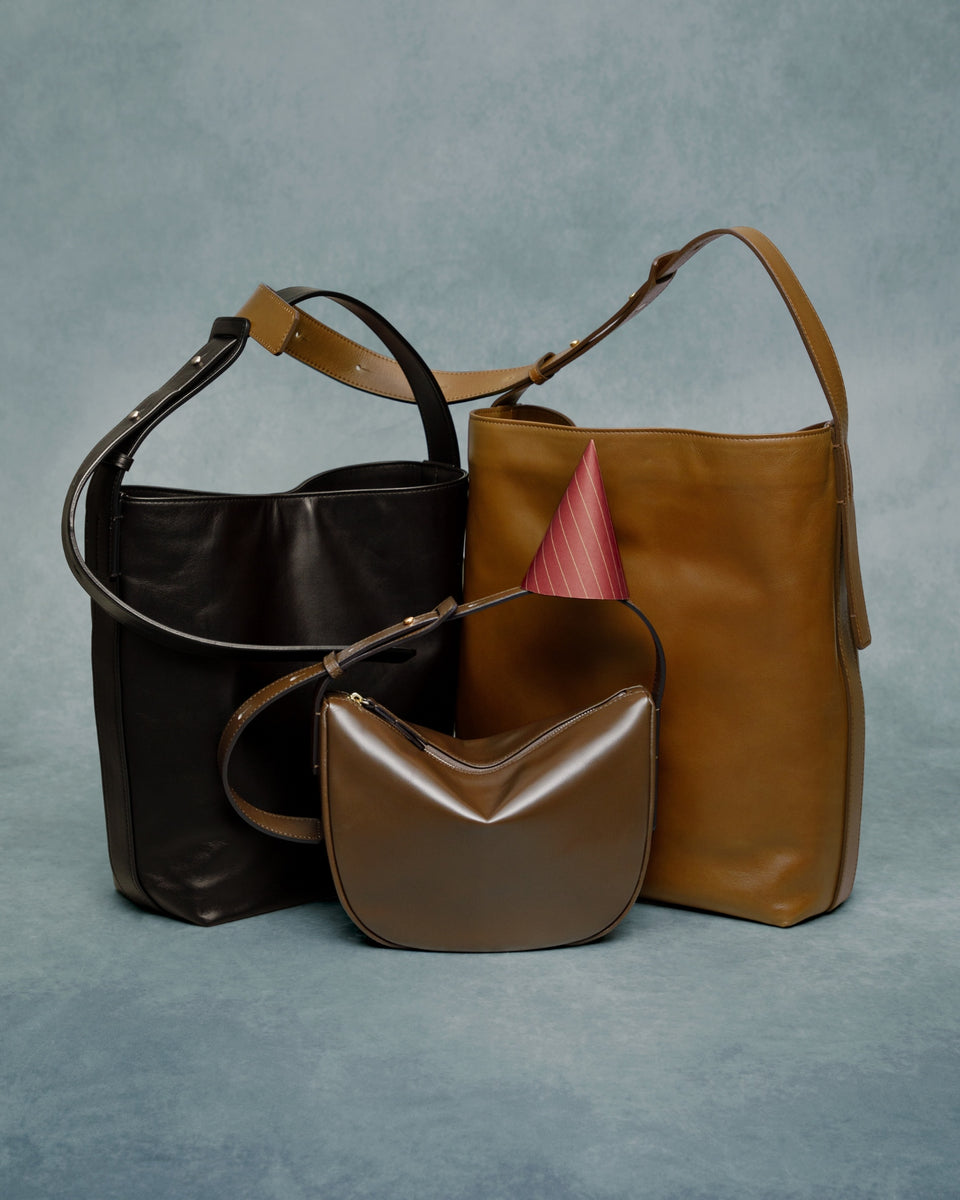 Three leather handbags in brown and black on a gray background