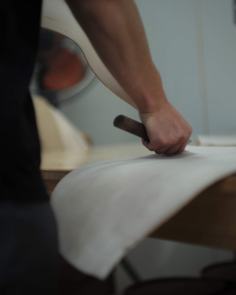 Skilled craftsman carefully cutting cordovan leather with a knife.