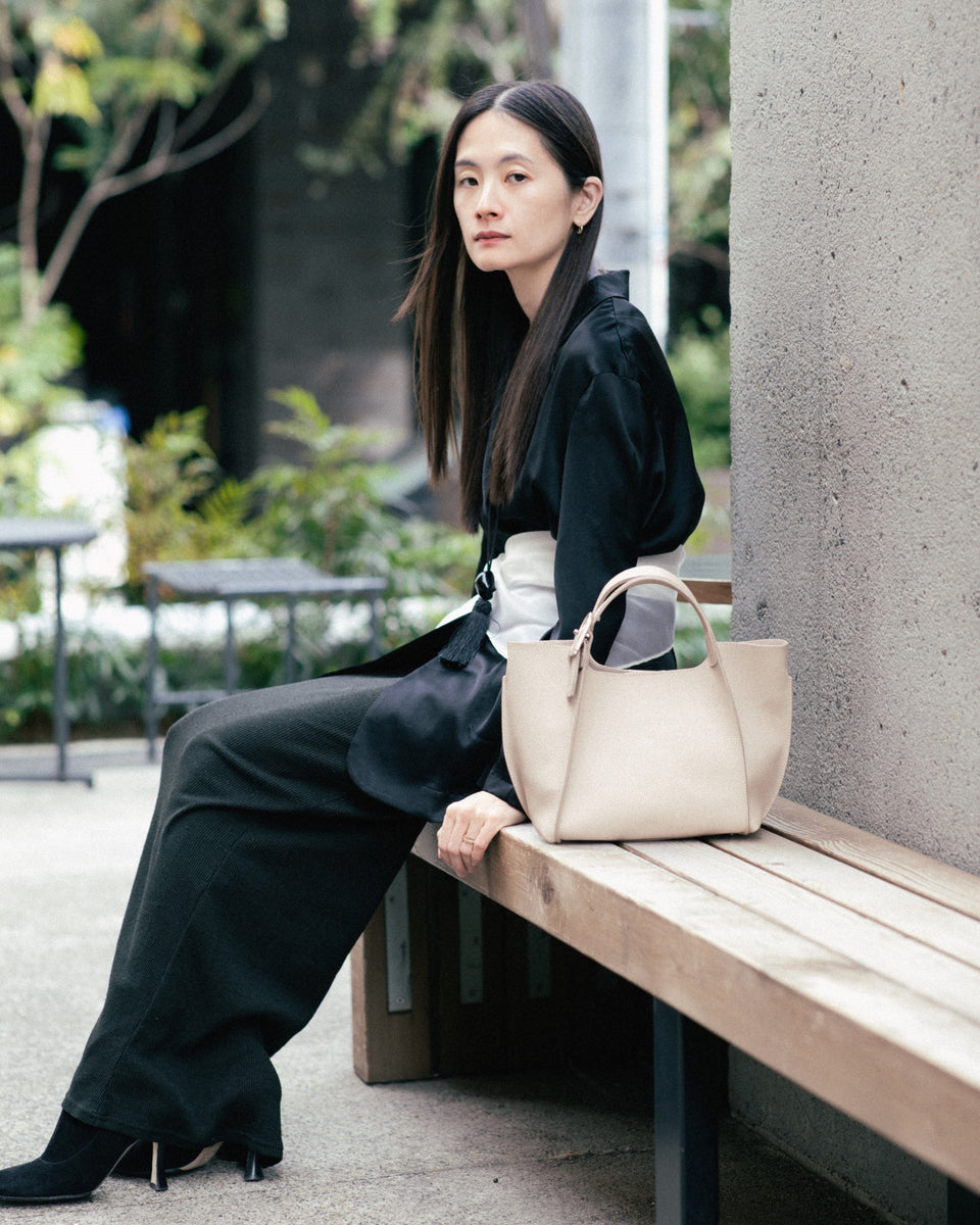 Woman sitting on a bench holding a beige leather bag in an outdoor setting