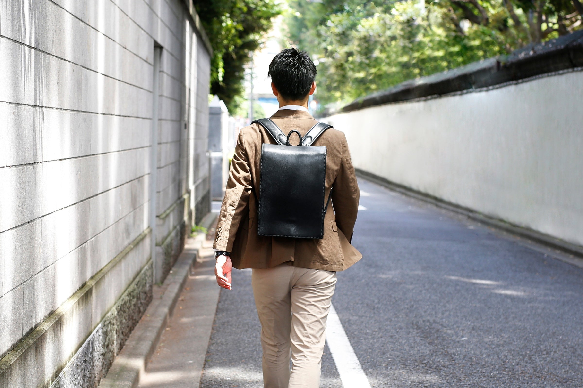 Man walking down a street with a black leather backpack: OTONA RANDSEL