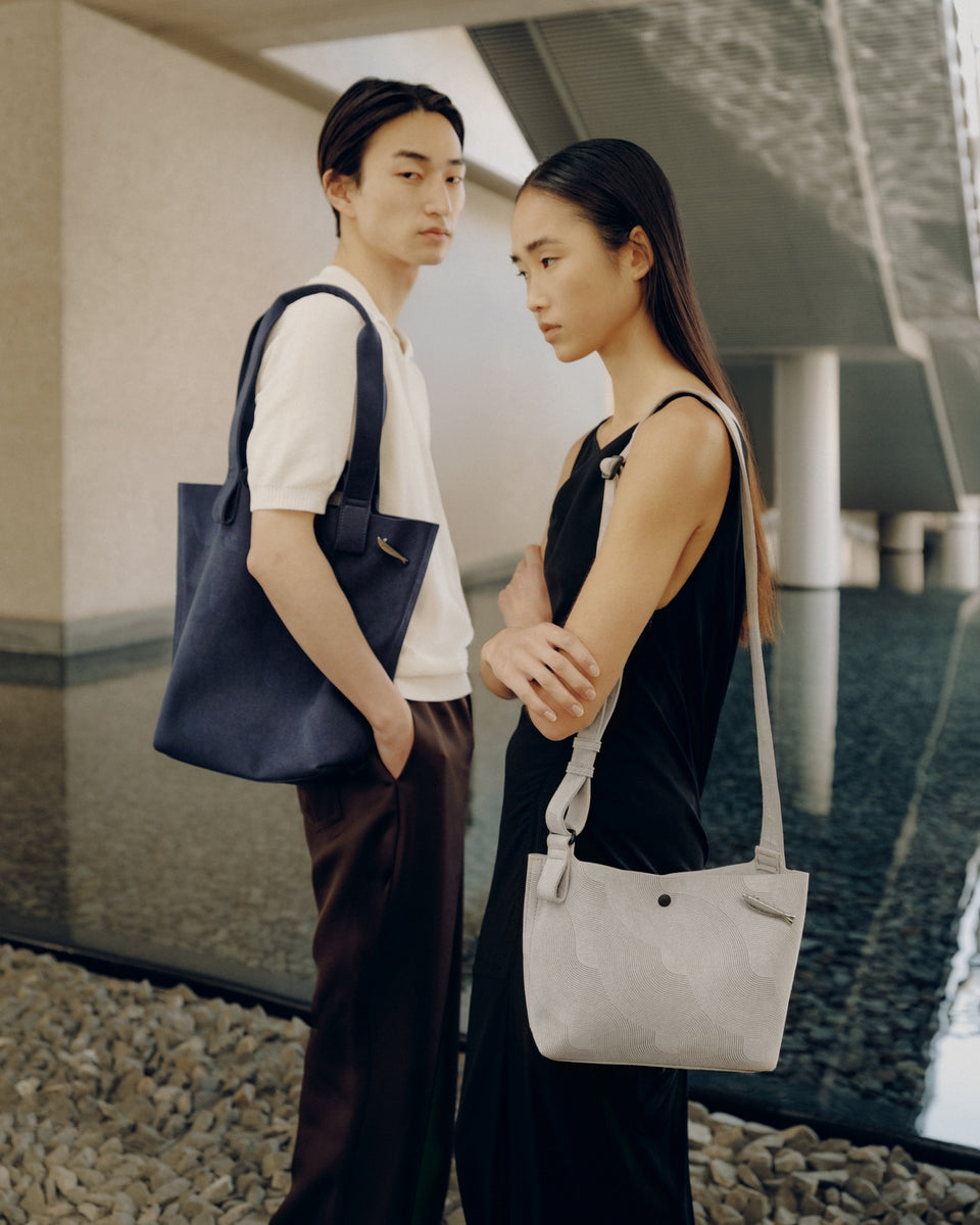 Two people standing outdoors, each holding a JAPANMOTIF Nami Washable bags.
