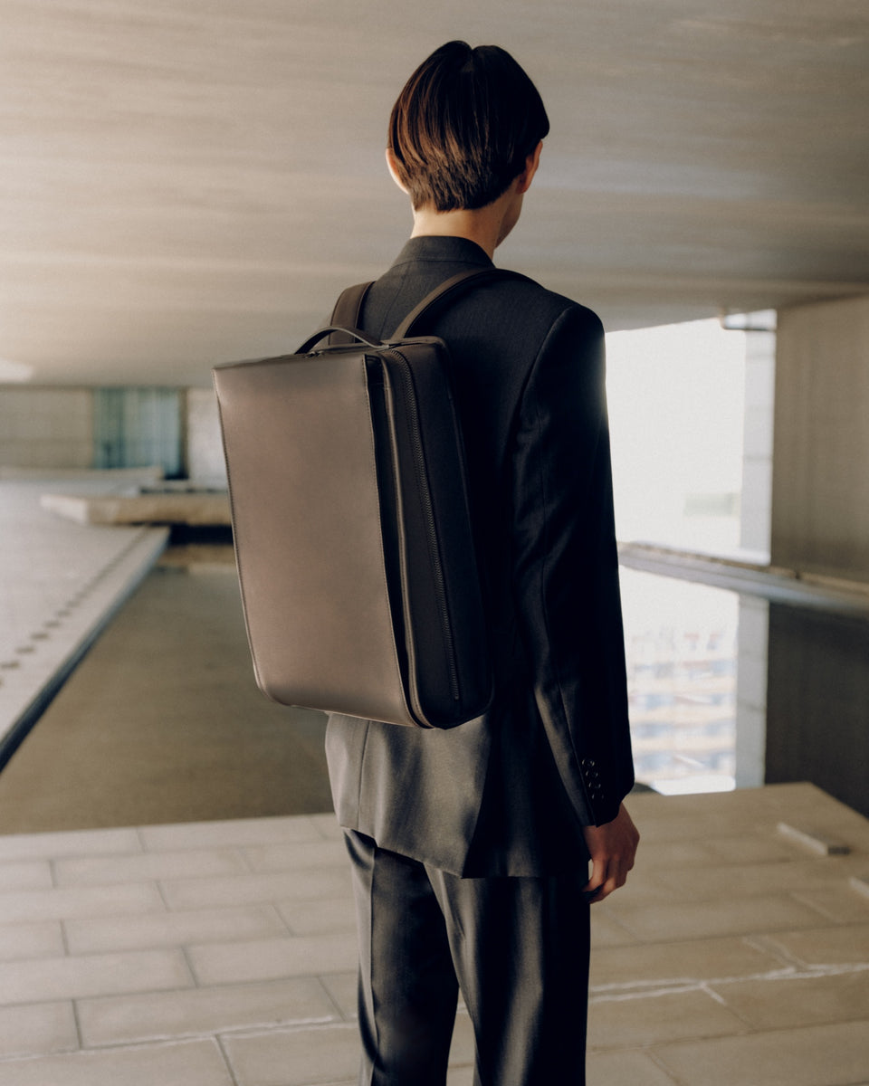 A man wearing a Vainno brown leather backpack in an indoor setting