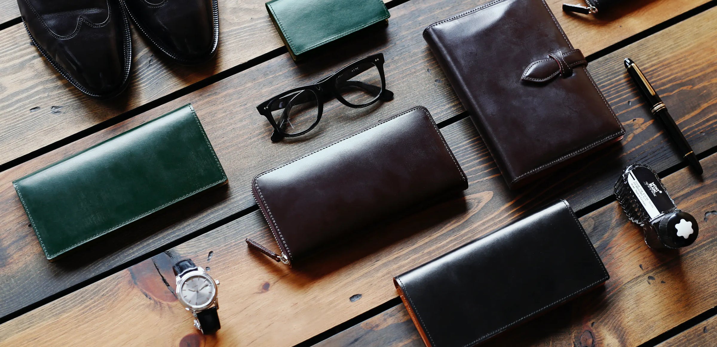 Collection of Bridle leather wallets, a watch, and glasses on a wooden surface