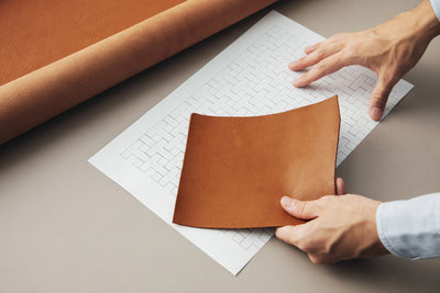 Image of a hand holding a piece of leather against a design drafted on paper.