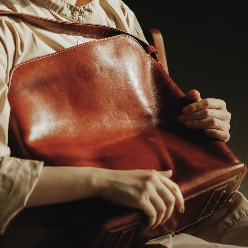 Person holding a brown leather bag against a dark background