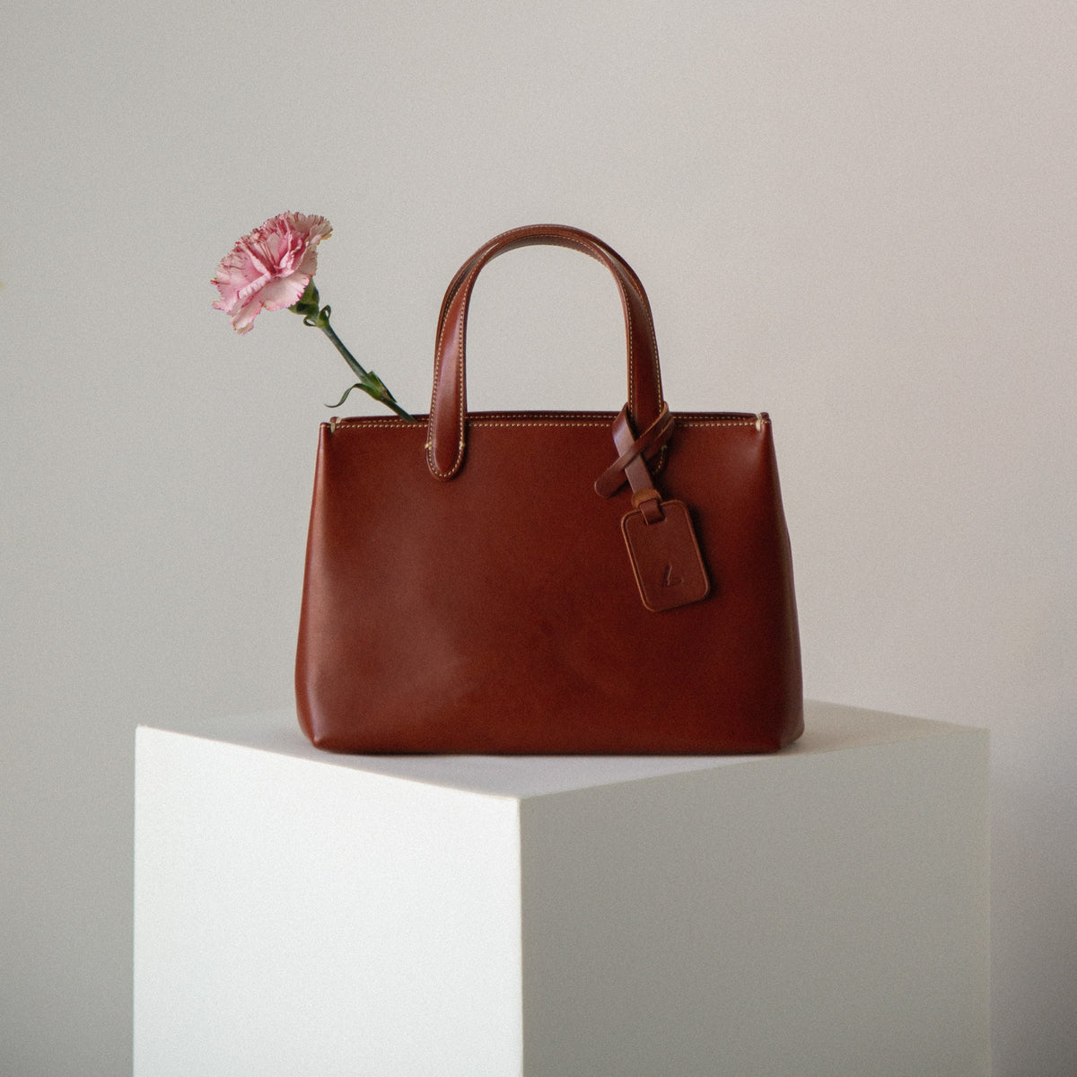 Brown leather handbag with a pink flower on a light gray background