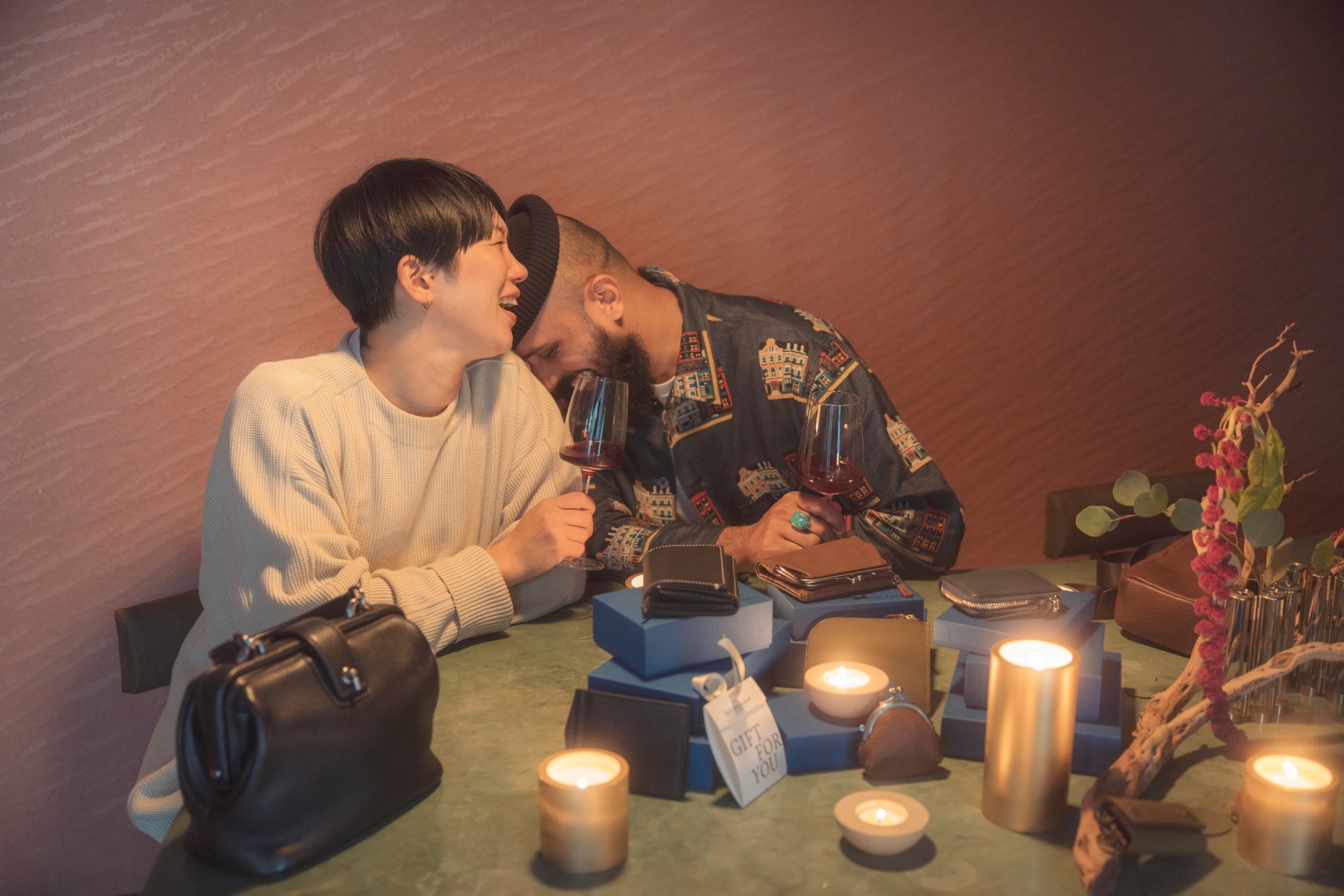 Two people sitting at a table with candles, decorative items, and Tsuchiya Kaban's leather bags engaged in conversation.