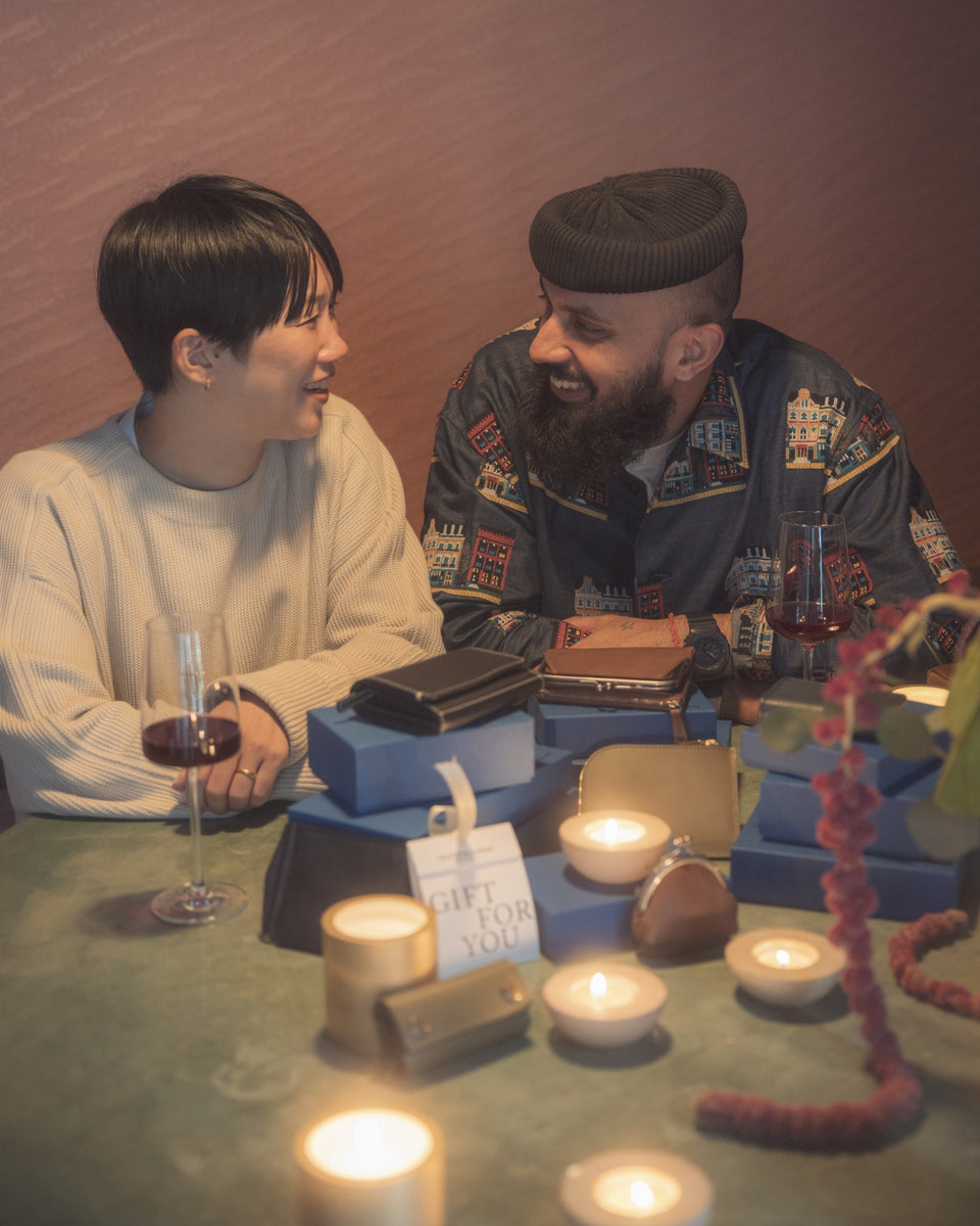 Two people sitting at a table with candles, decorative items, and Tsuchiya Kaban's leather bags engaged in conversation.