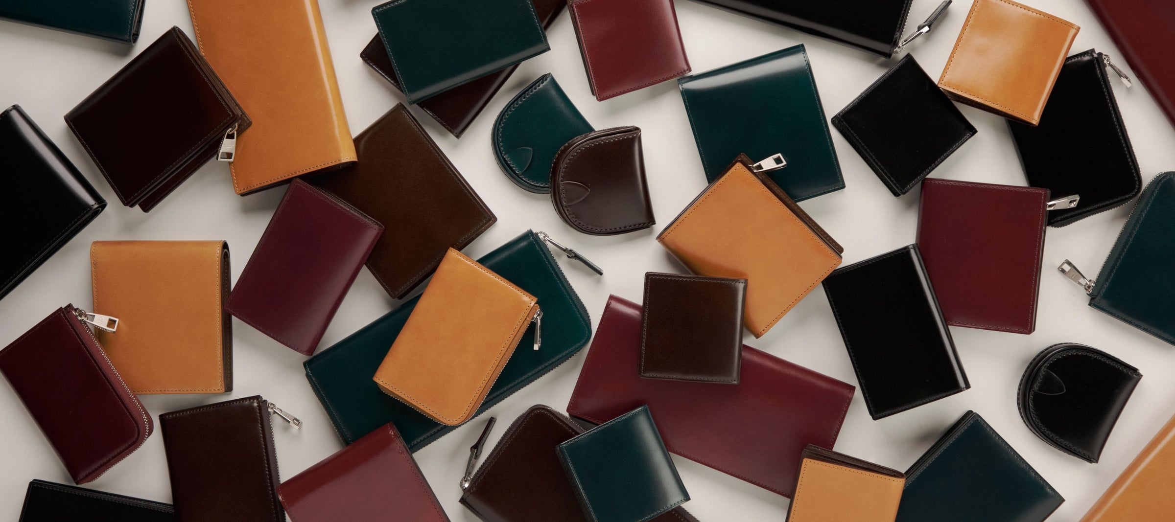 Collection of various colored Cordovan leather wallets on a white background
